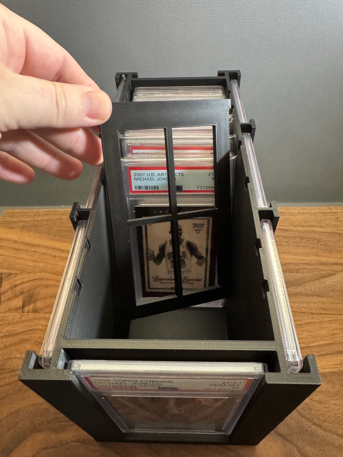 Hand lifting the adjustable divider out of the Slab Station Large, with a PSA-graded Michael Jordan Artifacts slab stored inside