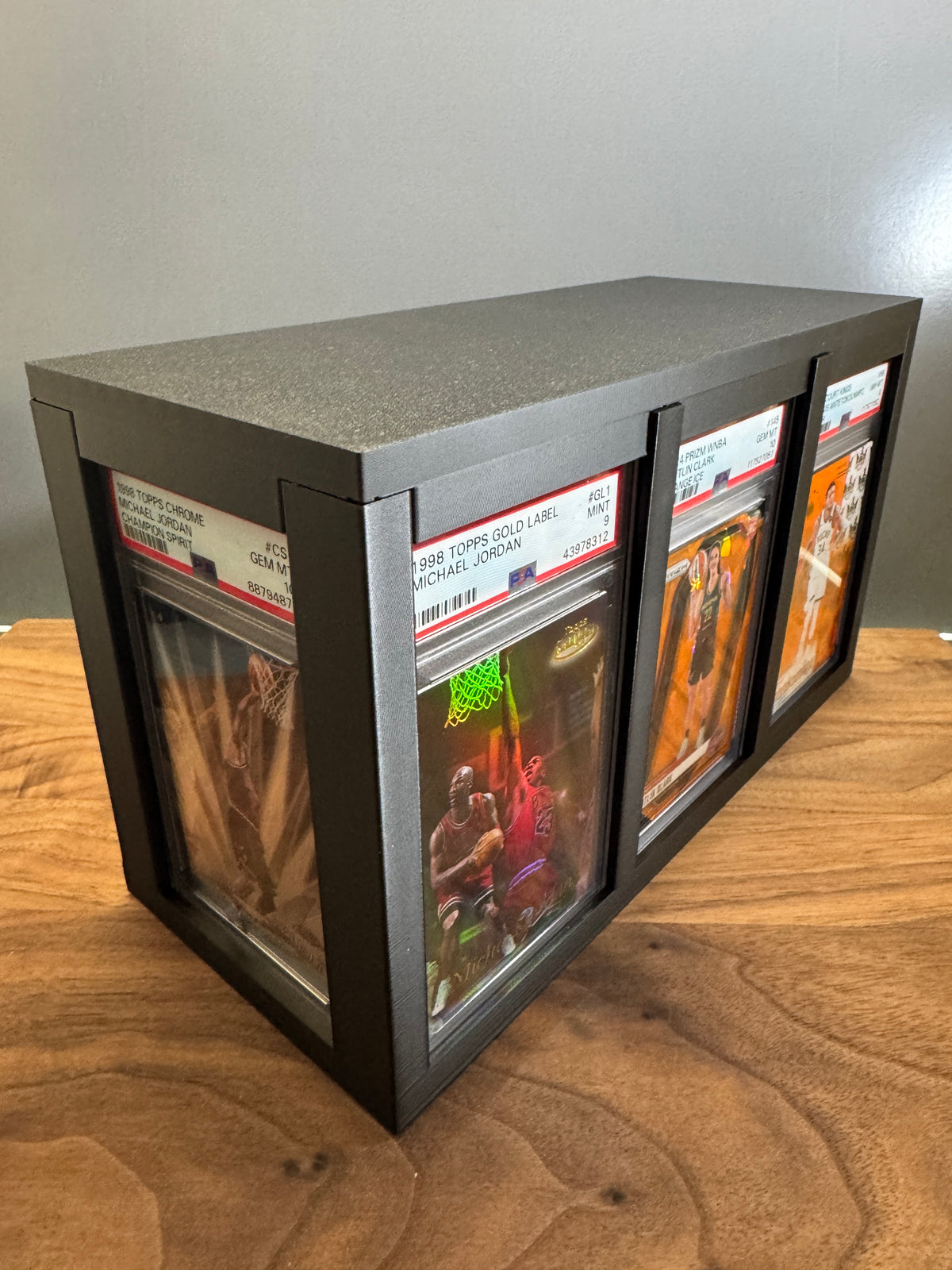 Slab Station Large graded card display box in black, angled view showing PSA-graded Michael Jordan slabs on the long side and a Caitlin Clark slab on the end panel